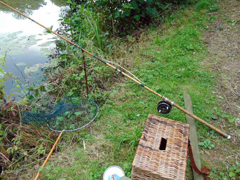Picture of a vintage split cane rod in a rod rest along side a wicker creel and a vintage landing net